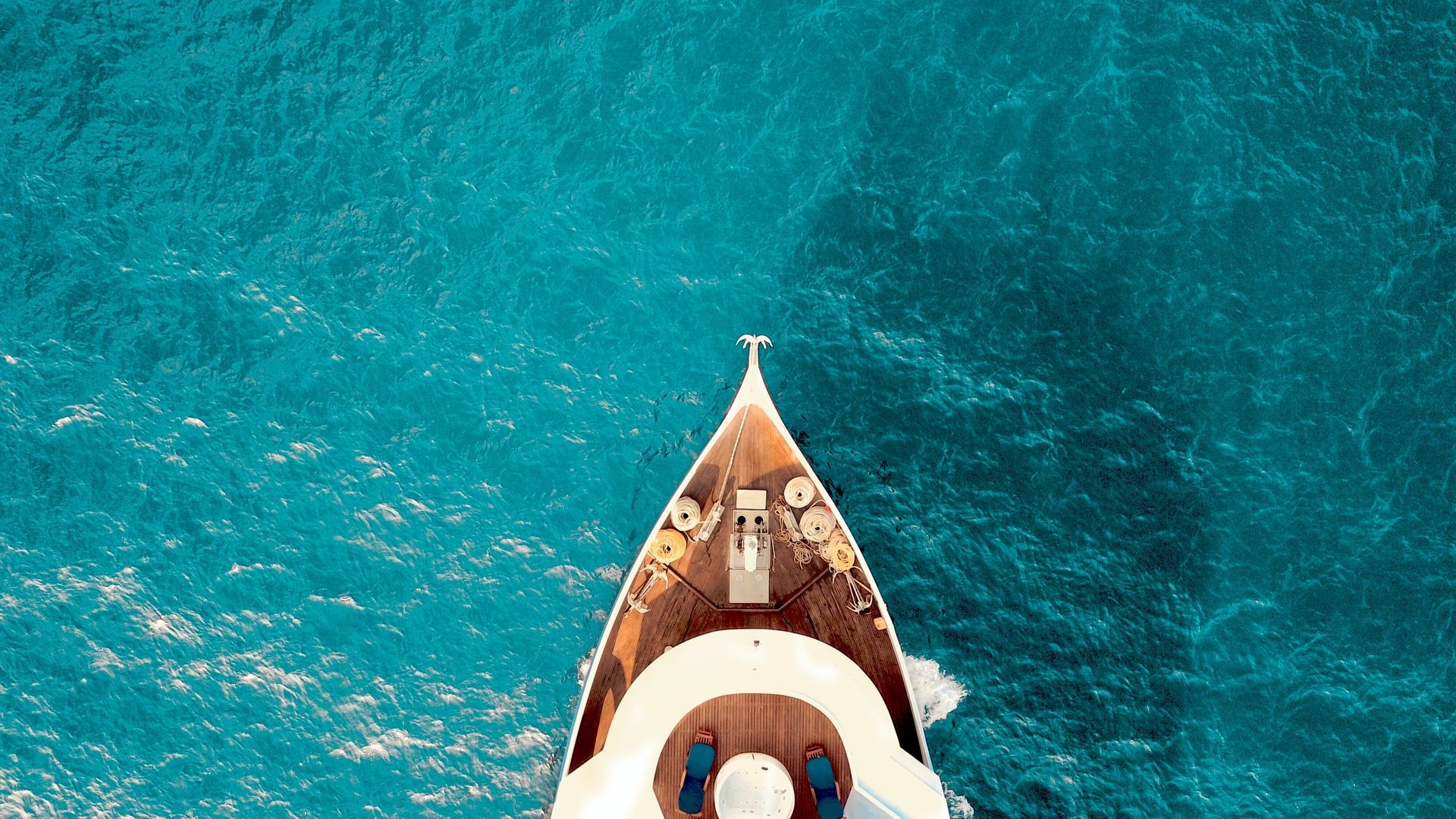 Aerial view of a boat's bow navigating through vibrant blue ocean waters.